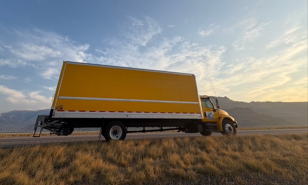 Camión amarillo de JW Delivery Corp en carretera junto a las montañas