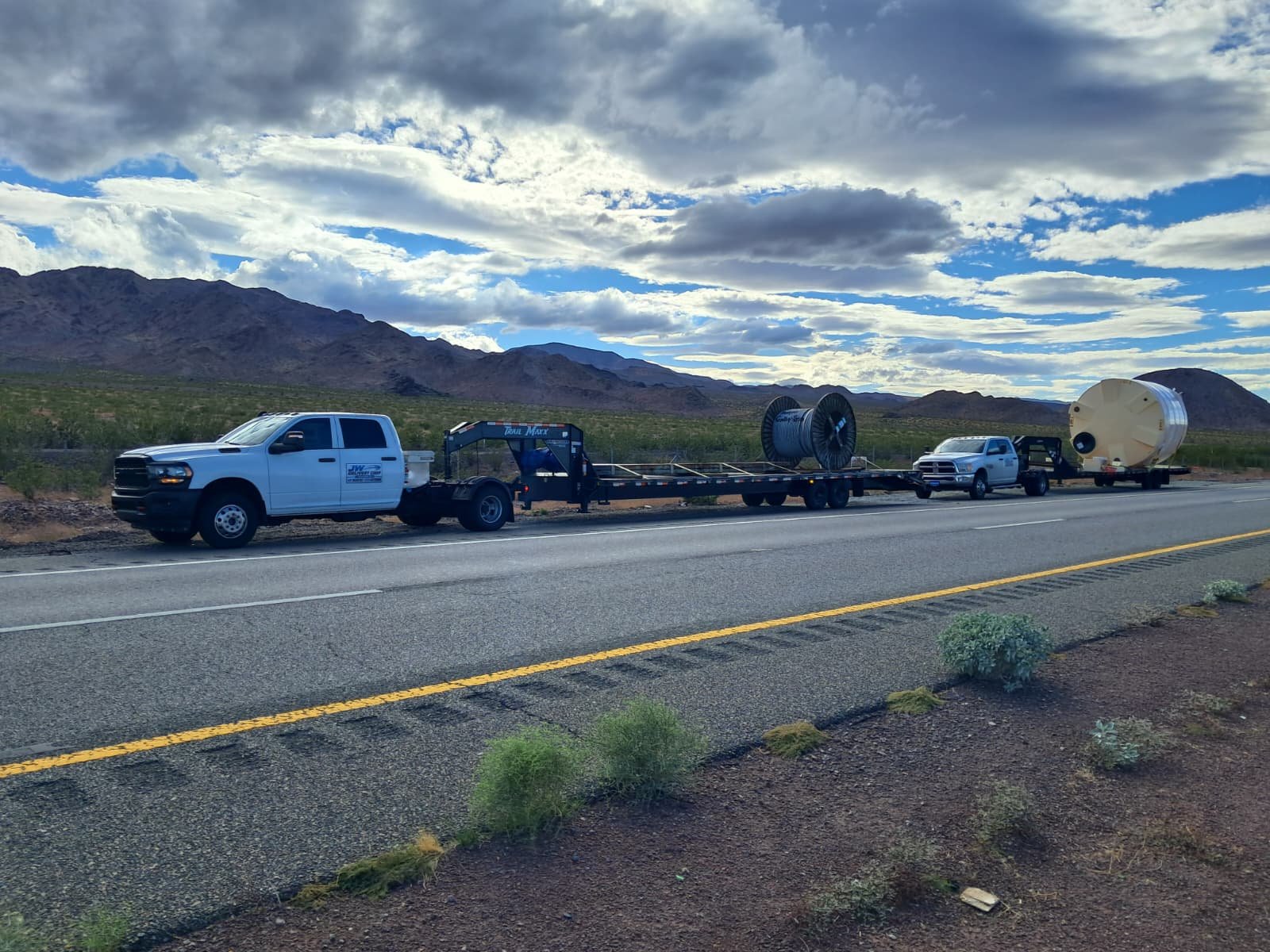 Los dos camiones de Francis S. e Isacc V., con remolques cargados, estacionados junto a una carretera de paisaje montañoso.